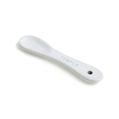 White ceramic spoon with "TEMPLE" engraving.
