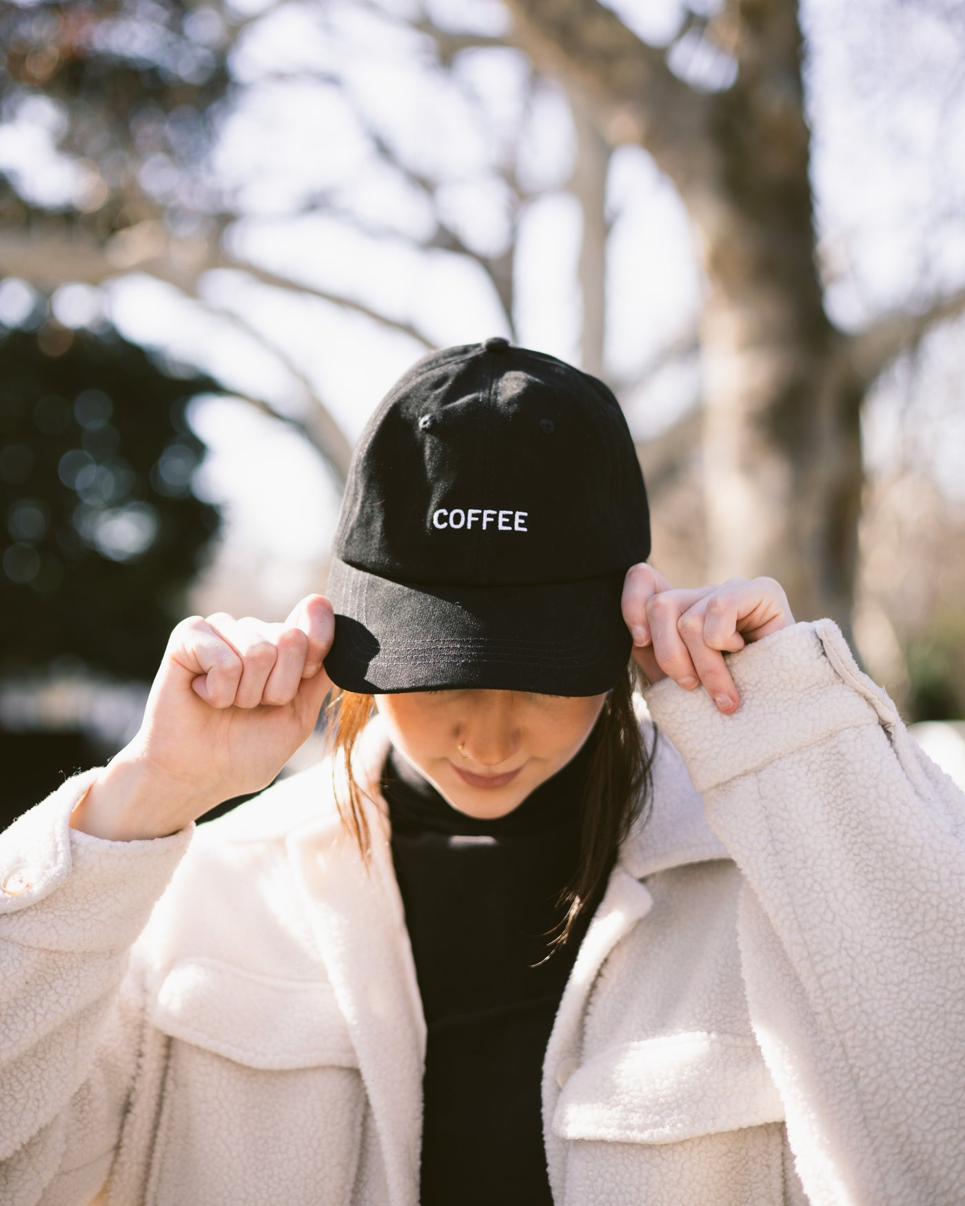 Person wearing a black cap with 'COFFEE' text outdoors