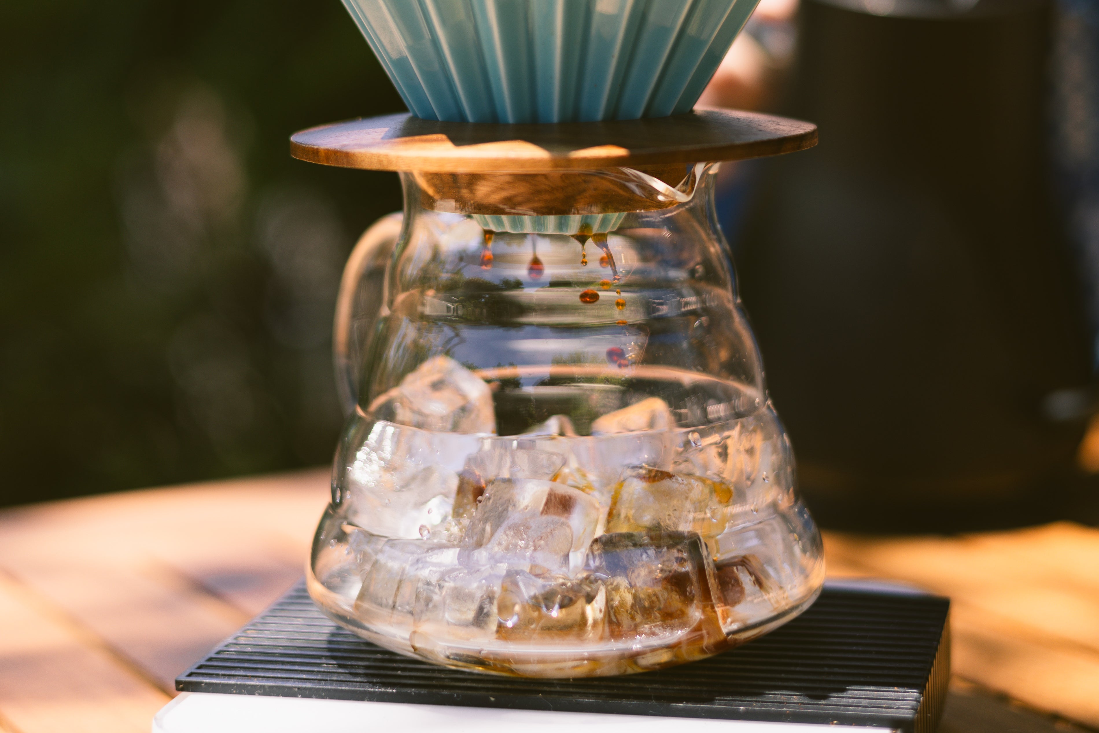 Close-up of coffee dripping from an Origami filter into a glass pitcher filled with ice, sitting on a coffee scale during the flash brew process.