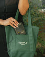 A person carries a green Temple Coffee canvas tote bag with cream-colored branding, holding a vintage Sony Walkman in the front pocket.