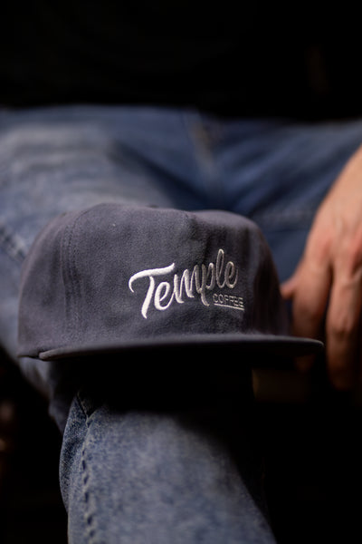 Dark cap with 'Temple Coffee' logo on a person wearing blue jeans.