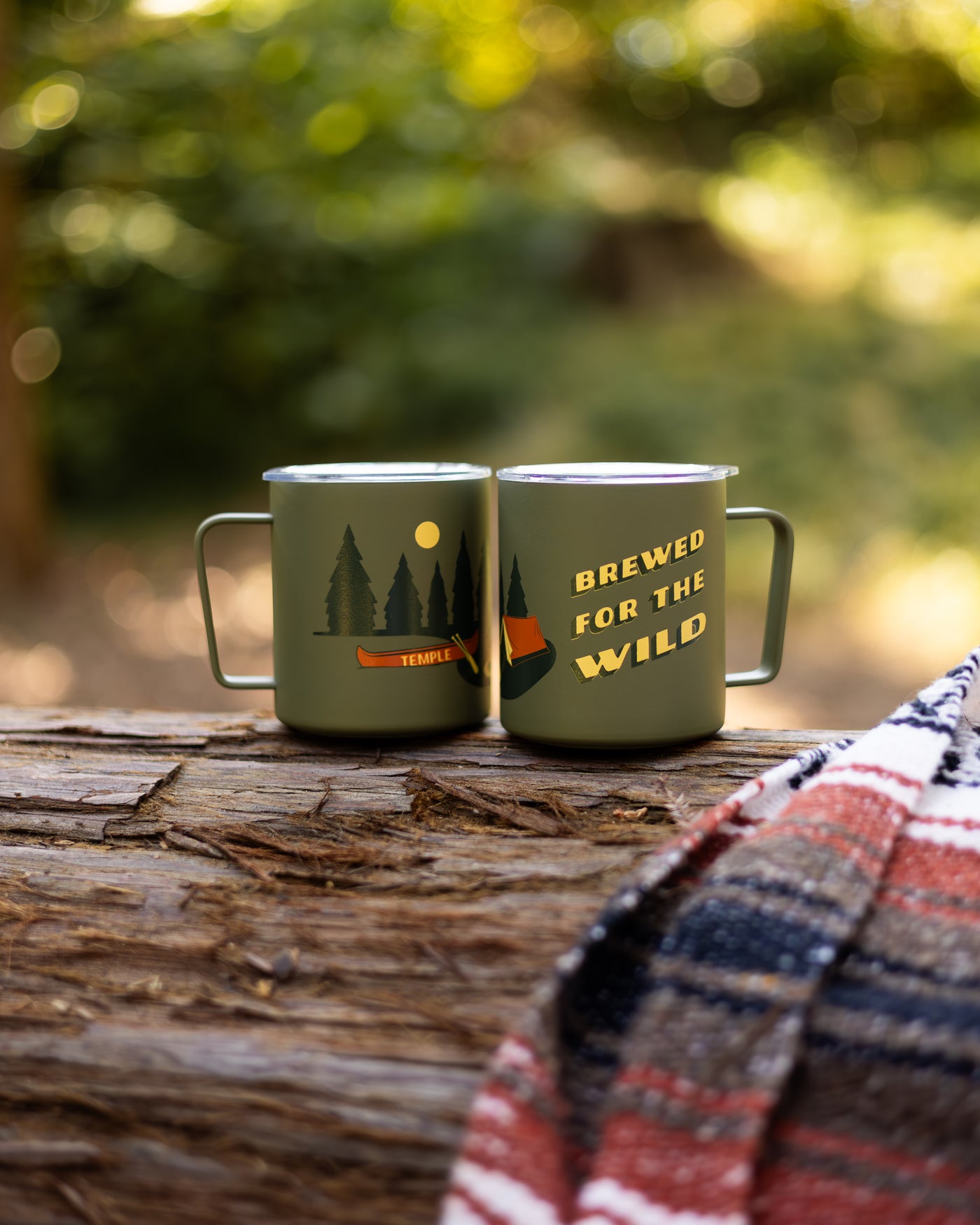 Two green mugs with nature-themed designs on a log outdoors.