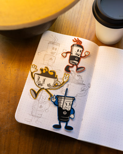 Open notebook with cartoon character stickers on a wooden surface with a coffee cup.