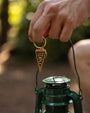 Hand holding a green lantern with a keychain featuring a pennant flag, against a blurred natural background.
