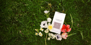 A bag of Lotus Blend coffee resting on lush green grass, surrounded by vibrant blooming flowers.