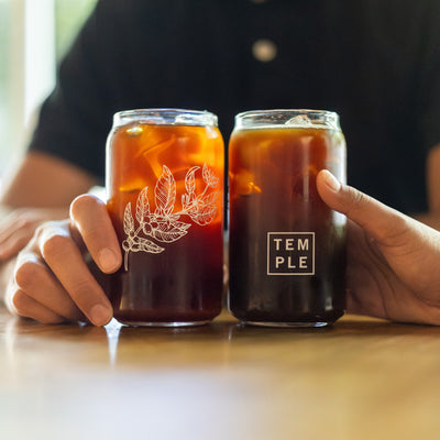 Hands holding two glass cans filled with cold brew coffee.