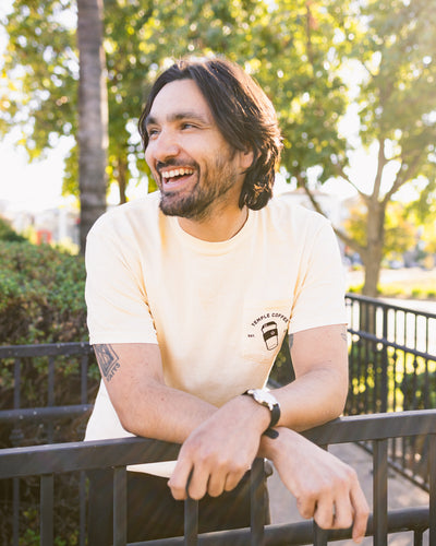 Person wearing a cream-colored T-shirt with a to-go cup graphic and text on the front pocket.