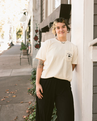 Person wearing a cream-colored T-shirt with a to-go cup graphic and text on the front pocket.