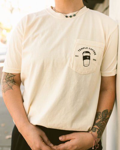 Person wearing a cream-colored T-shirt with a to-go cup graphic and text on the front pocket.