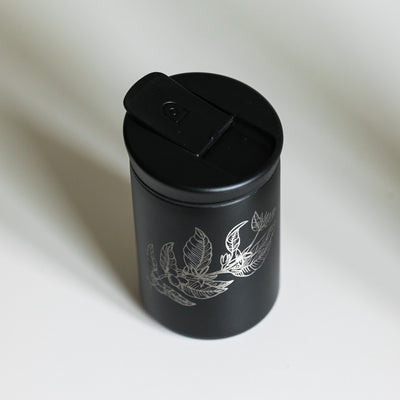 Black tumbler with an engraved plant design on a white background.