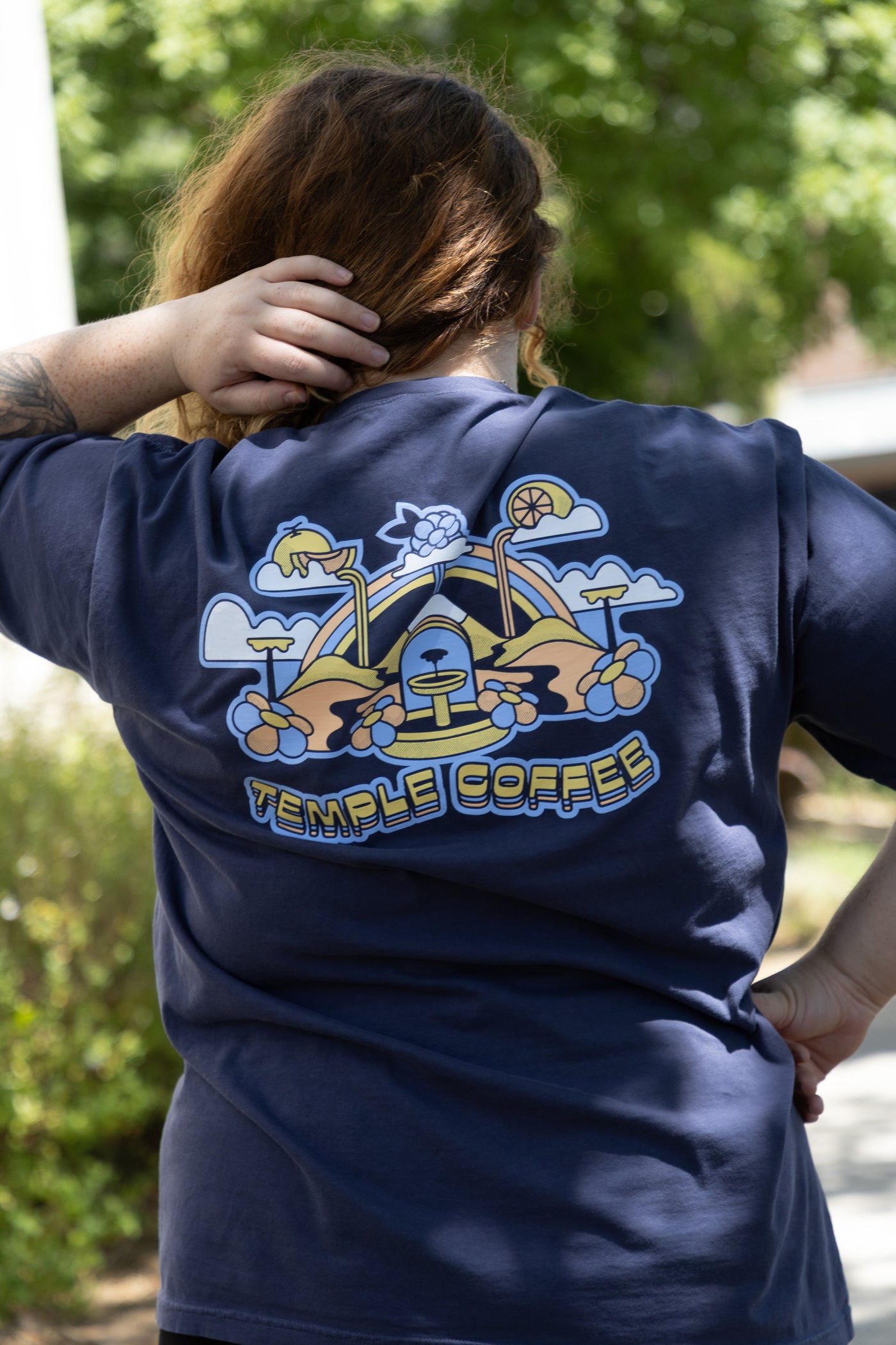 Person wearing a navy blue t-shirt with 'Temple Coffee' logo on the back, standing outdoors.