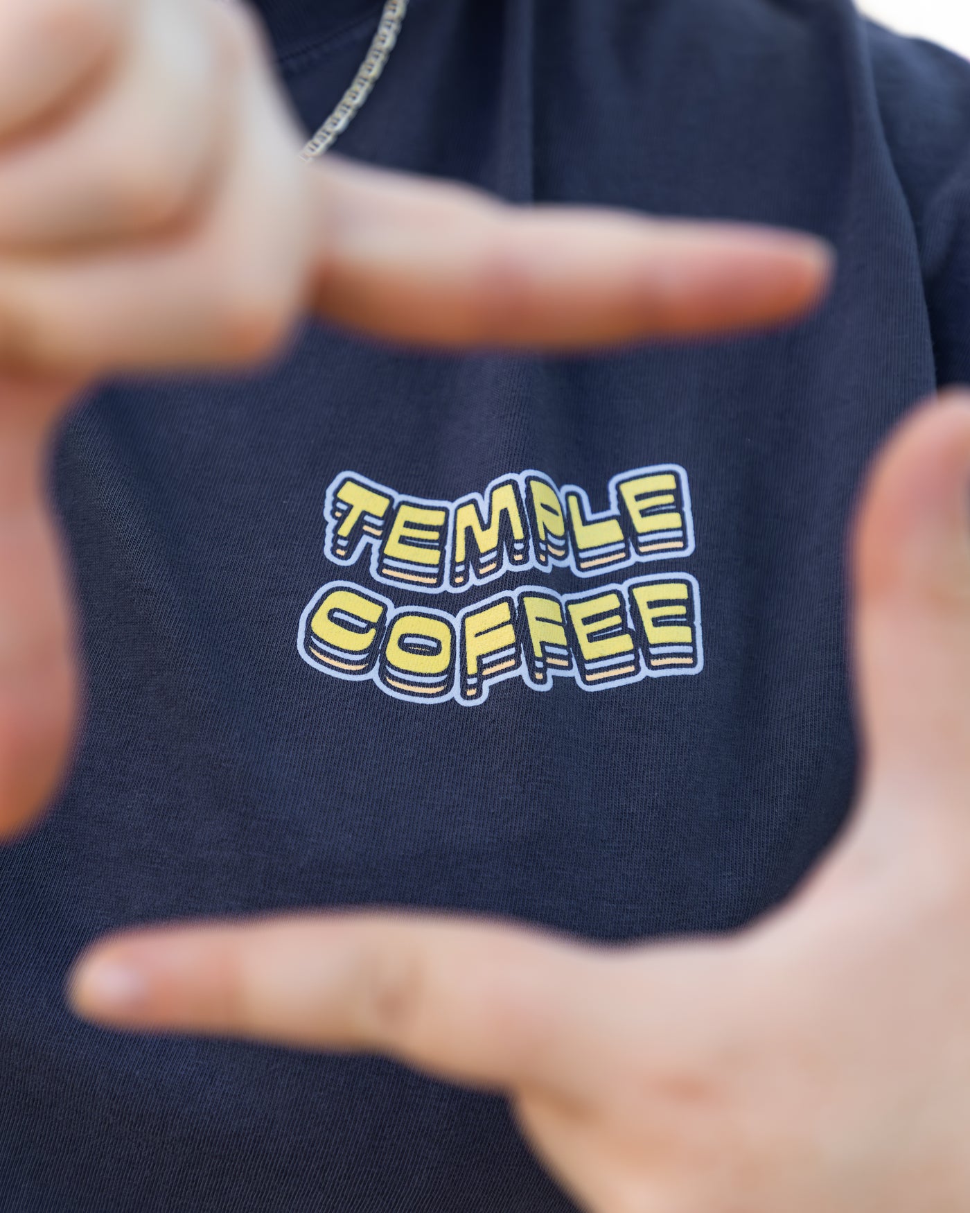 Navy shirt with 'Temple Coffee' text framed by a person's hands
